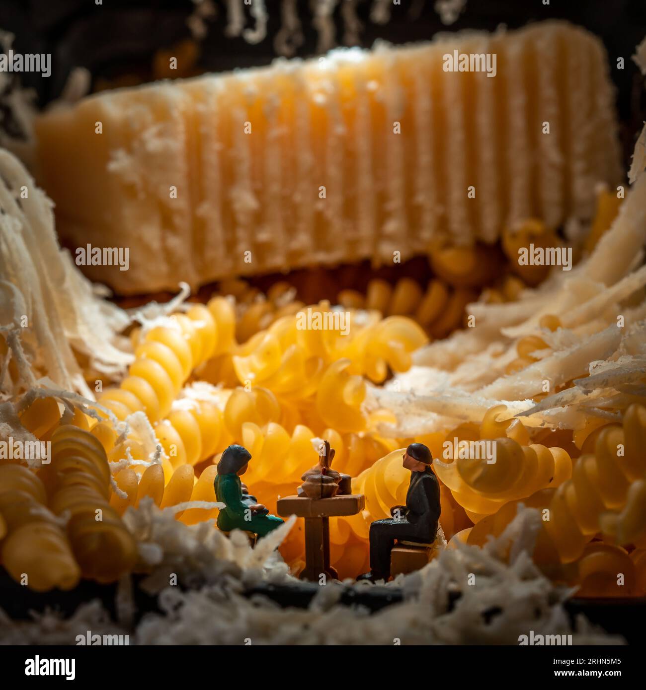 Miniatur-Paar sitzt am Esstisch, umgeben von geriebenem Käse, ein konzeptionelles Bild für den jüdischen Feiertag von Shavuot - Pfingsten Stockfoto