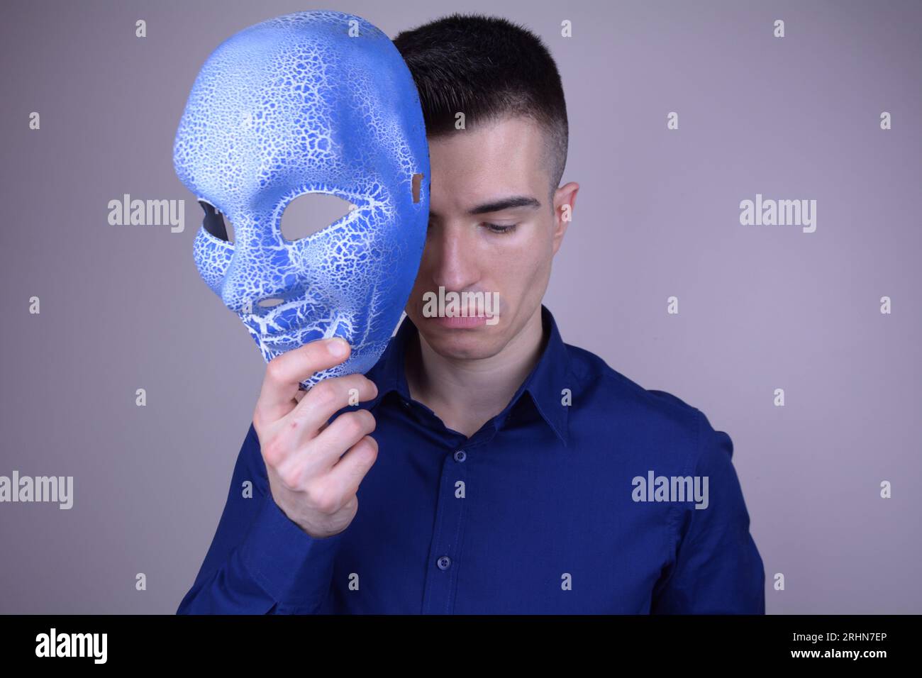 Trauriger eleganter Mann, der eine Maske vor seinem Gesicht auf isoliertem Hintergrund hält Stockfoto