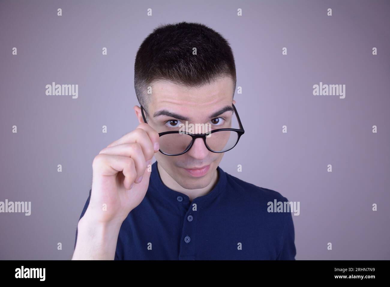 Der junge Mann zieht seine Brille an, schaut aufmerksam auf den Betrachter, isolierter Hintergrund Stockfoto