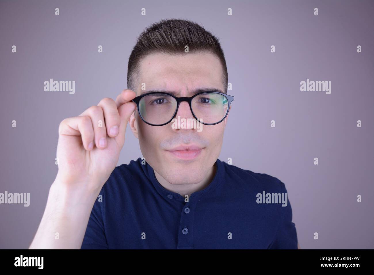 Der junge Mann zieht seine Brille an, schaut aufmerksam auf den Betrachter, isolierter Hintergrund Stockfoto