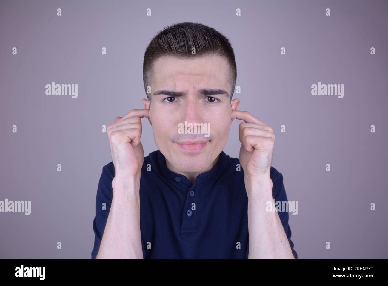 Gutaussehender Kaukasier, der Ohren mit Fingern auf isoliertem Hintergrund bedeckt Stockfoto