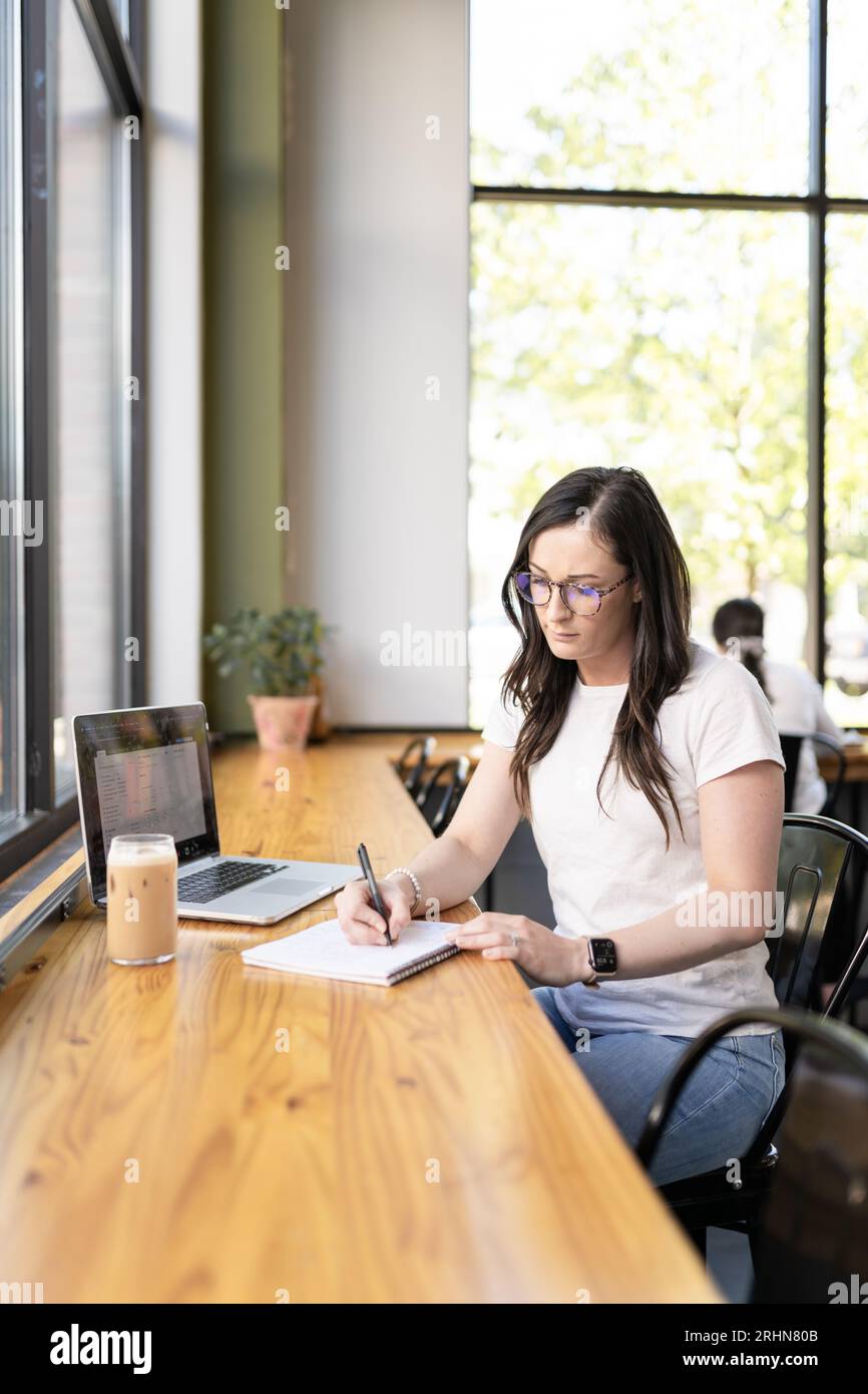 Eine Frau, die Eiskaffee trinkt, schreibt in ihr Notizbuch Stockfoto