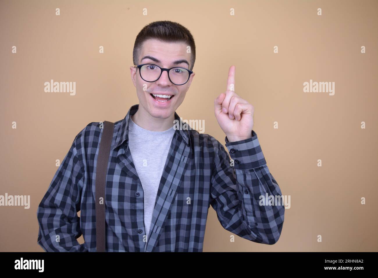 Kaukasischer junger gutaussehender lächelnder Student in der Brille hält den Finger in der „Eureka“-Geste hoch Stockfoto