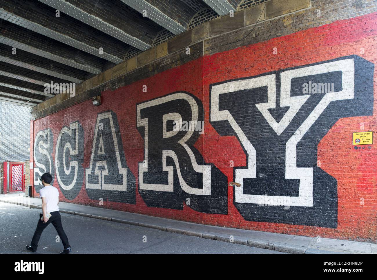 Auffälliges typografisches „GRUSELIGES“ Wandbild unter einer Eisenbahnbrücke in Shoreditch, East London, mit einem Fußgänger, der in einer ruhigen Straße vorbeiläuft. Stockfoto