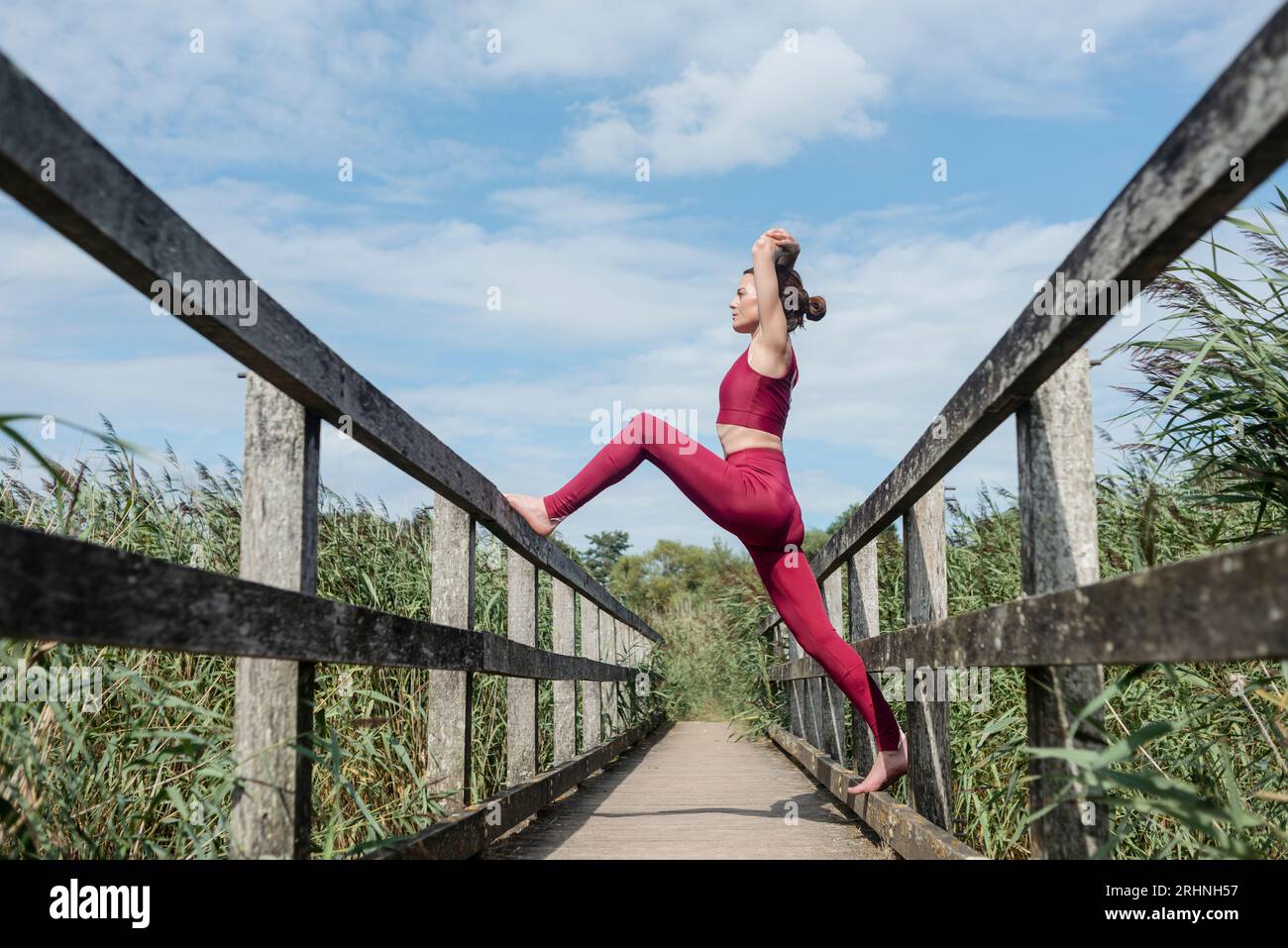 Eine sportliche Frau, die auf einer Holzbrücke eine Yoga-Position mit hohem Ausfallschritt macht Stockfoto