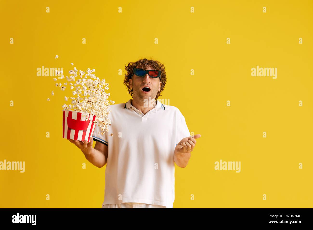 Reifer emotionaler Mann in 3D-Brille mit Popcorn-Korb, der beeindruckende Filme vor gelbem Studiohintergrund ansieht Stockfoto