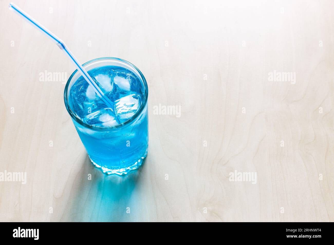 Oben Blick auf den blauen alkoholischen Cocktail im Glas mit Eis und Trinkhalm auf hellem Tisch mit Textabschnitt Stockfoto