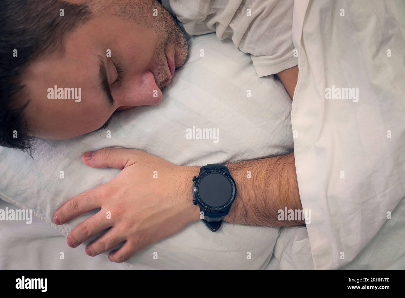 Heartbeat-Überwachung mit einem intelligenten Gadget im Traum. Der Mann schläft auf einem weißen Kissen mit einer Smartwatch am Handgelenk, um seinen Herzschlag zu überwachen. Ein leeres scr Stockfoto