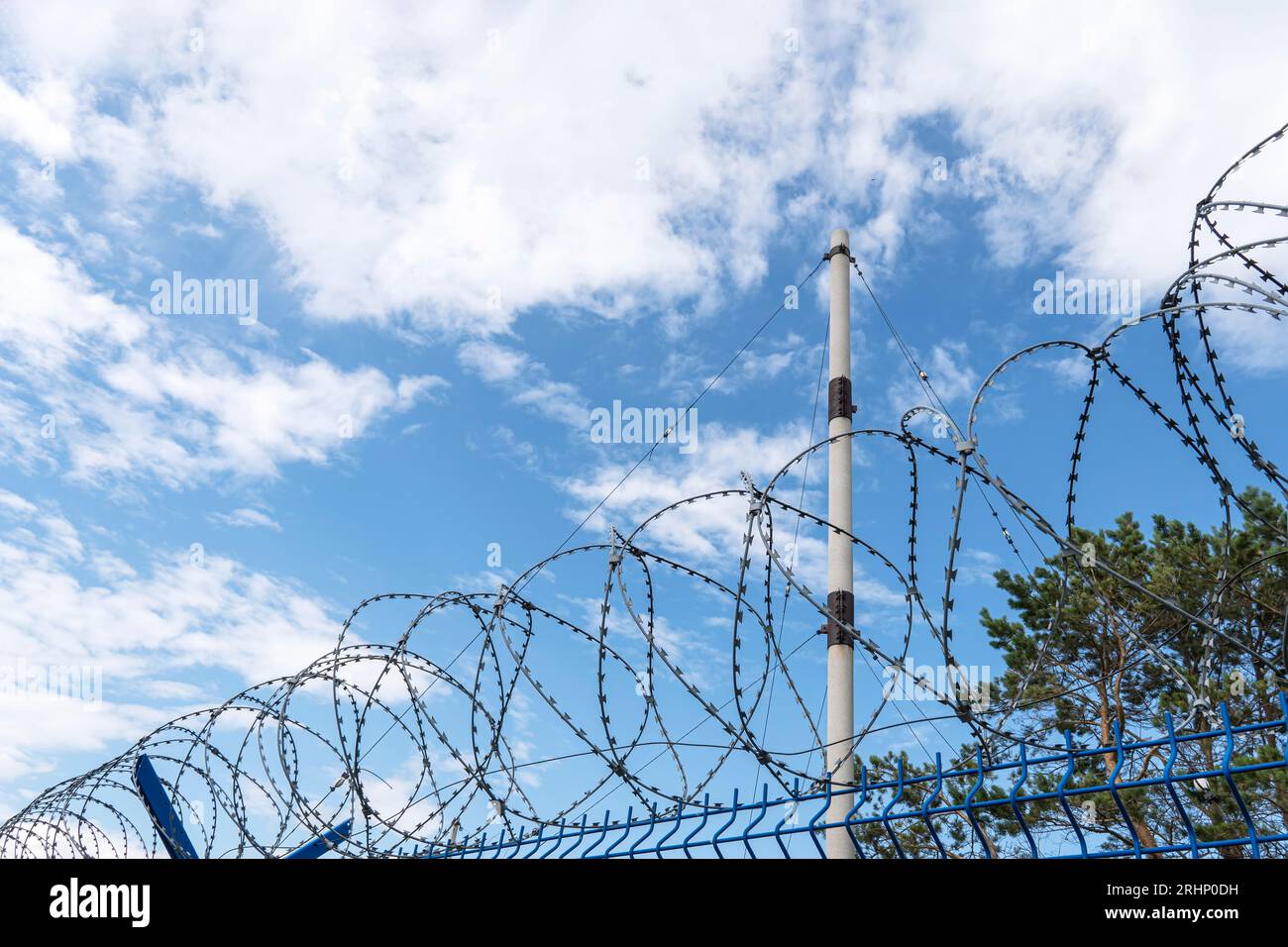 Stacheldraht gegen bewölkten Himmel, Nahaufnahme. Metallzaun mit Stacheldraht, im Freien Stockfoto
