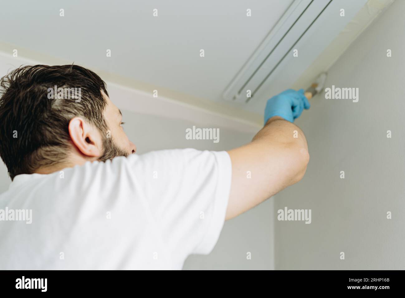 kaukasischer bärtiger Mann malte Wand mit Pinsel. Malerwohnung, renovierendes Haus mit grauer Farbe. Bild mit selektivem Fokus Stockfoto