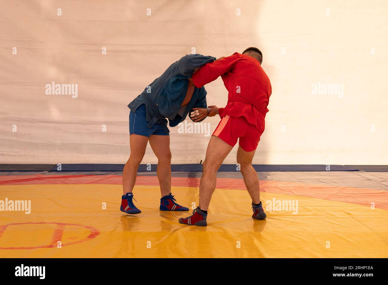 Zwei Männer in blauen und roten Strumpfhosen ringen auf einem gelben Tatami. Sambo-Wrestler trainieren. Sambo-Wettbewerb Stockfoto