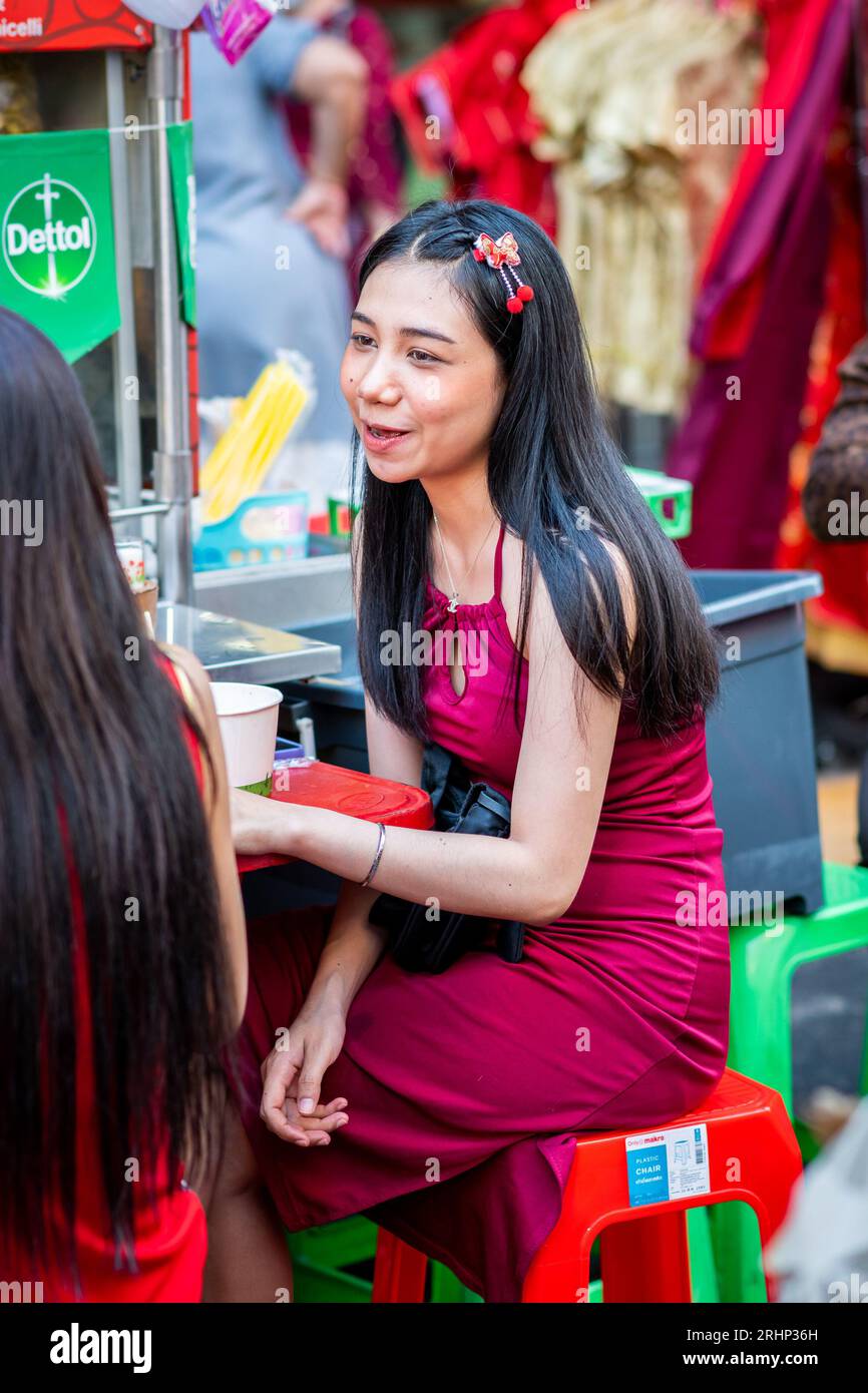 Ein wunderschönes thailändisches Mädchen plaudert mit ihrem Freund beim Mittagessen an einem Nudelspeisestände auf der Yaowarat Rd China Town, Bangkok, Thailand. Stockfoto
