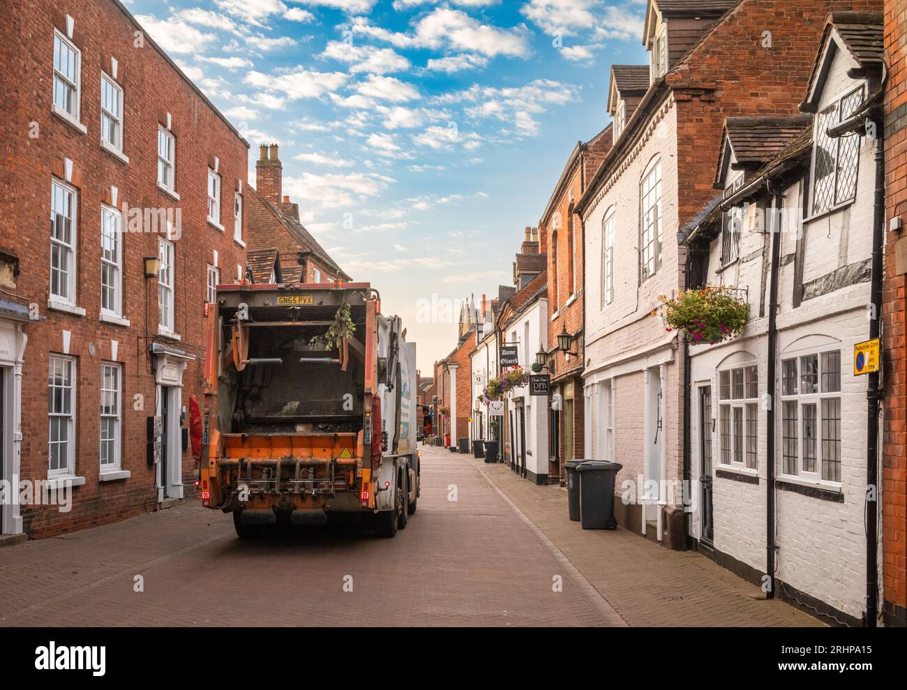Ein kommunales Müllsammelfahrzeug sammelt bei Sonnenaufgang in Dam Street, Lichfield, Staffordshire, UK, Müll oder Müll aus Mülltonnen. Stockfoto