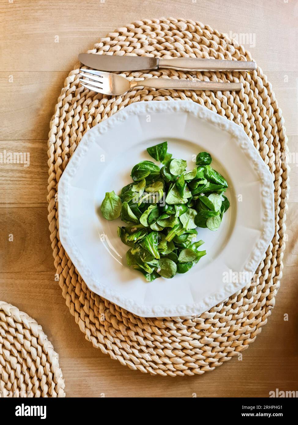 Feldsalat auf weißem Teller mit Besteck und Sitzecke, Thema gesunde Ernährung Stockfoto