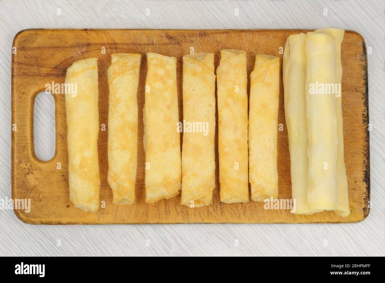 Hausgemachte Halbzeuge auf Holzbrett. Gefrorene Pfannkuchen mit Füllung, die zu Brötchen gedreht wird. Zubereitungen selbstgemachter Lebensmittel. Stockfoto