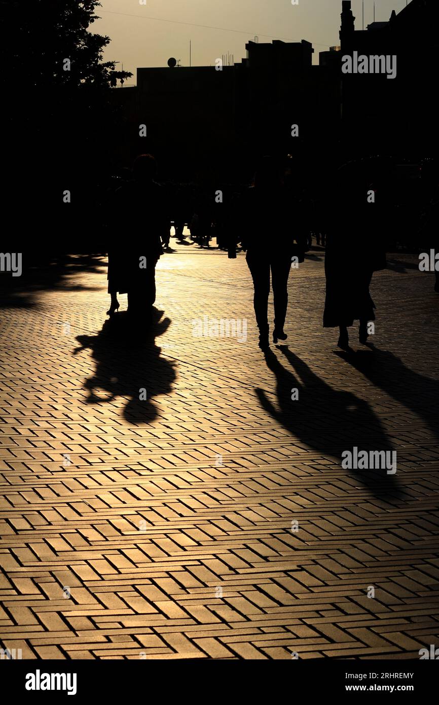 Tägliches Leben in Japan „Silhouetten von Menschen, die durch die Stadt spazieren, beleuchtet von der untergehenden Sonne“ Stockfoto