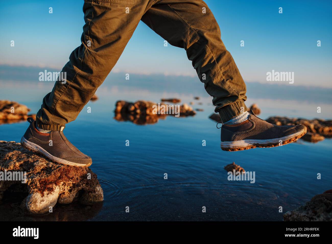 Junge läuft auf Steinen im See, Nahaufnahme auf Stiefel Stockfoto