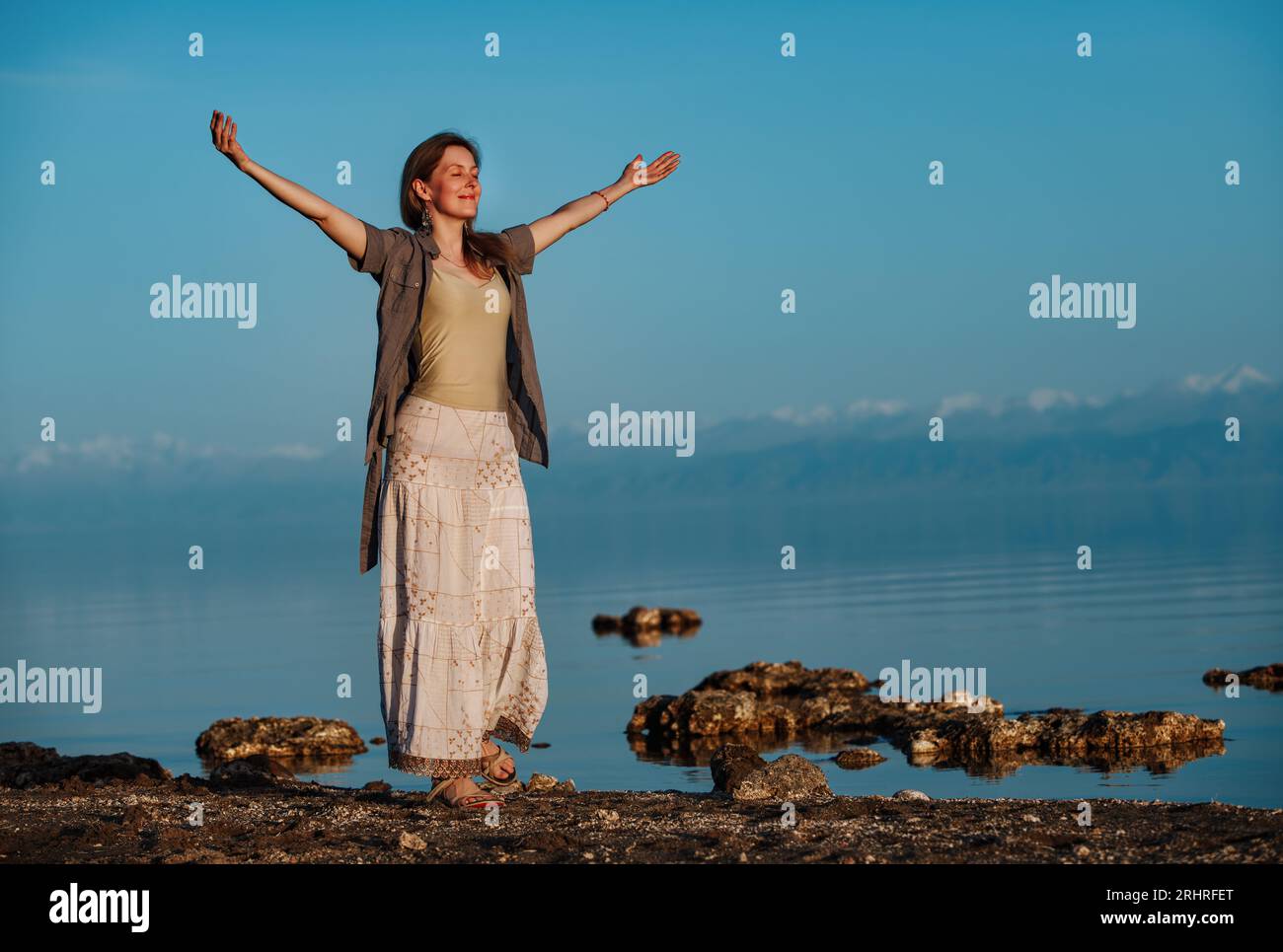 Schöne junge Frau, die mit geschlossenen Augen am Ufer des Sees steht Stockfoto