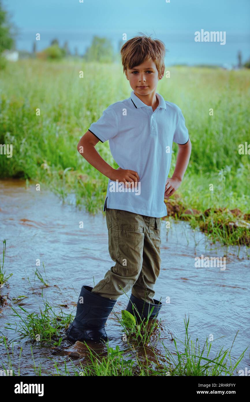 Junge in Gummistiefeln steht mitten in einem Bach Stockfoto