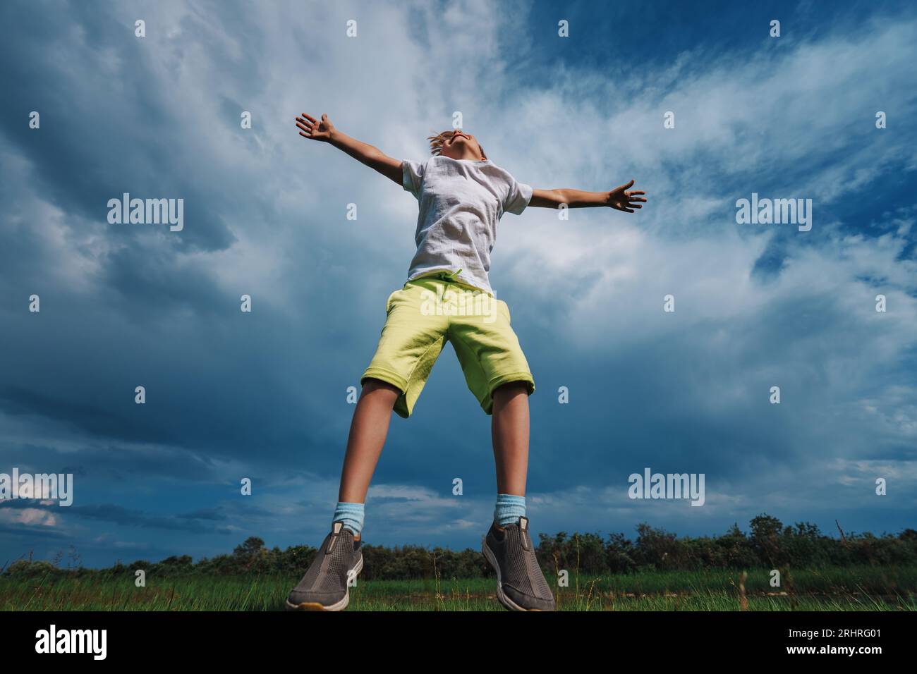 Glücklicher Junge, der auf dem Feld auf blauem Himmelshintergrund springt Stockfoto