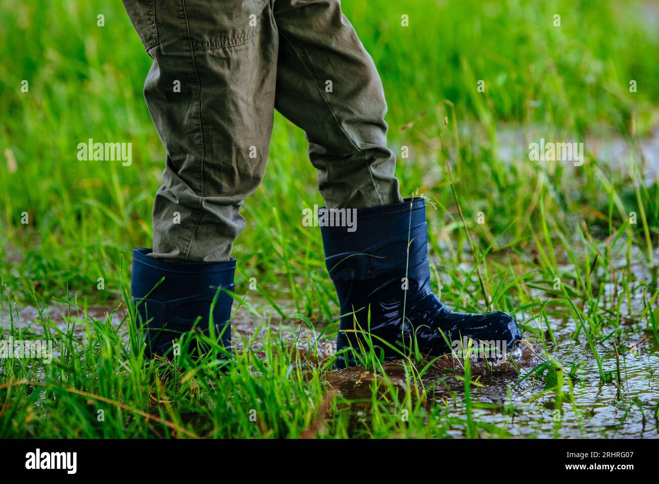 Junge in Gummistiefeln, die nach dem Regen auf nassem Gras laufen Stockfoto