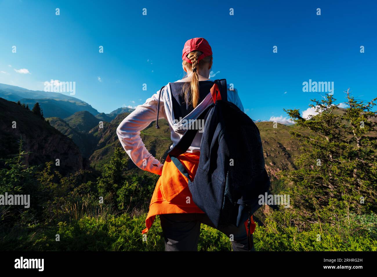 Eine junge Wanderin mit Rucksack steht auf einem Berg und schaut auf das Tal Stockfoto