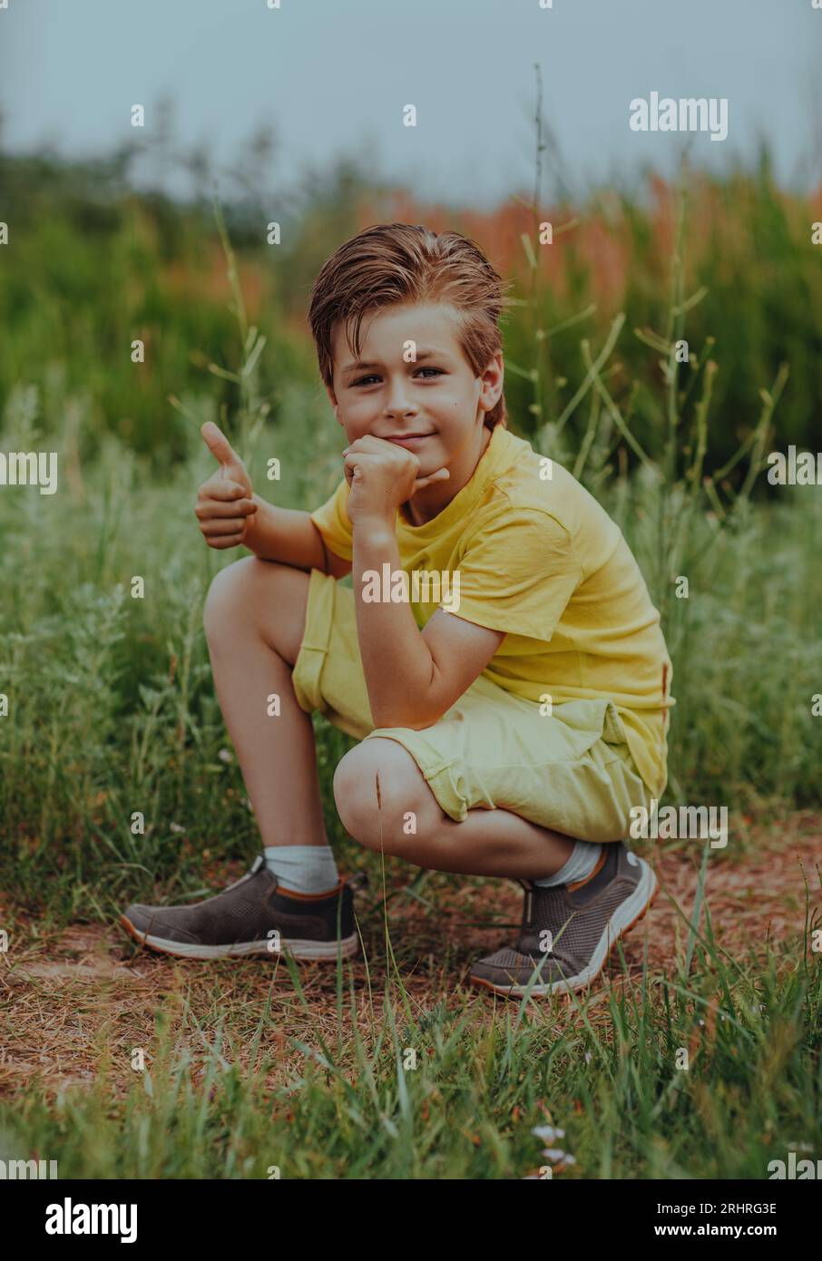 Happy Boy sitzt auf einer grünen Wiese und gibt einen Daumen nach oben Stockfoto