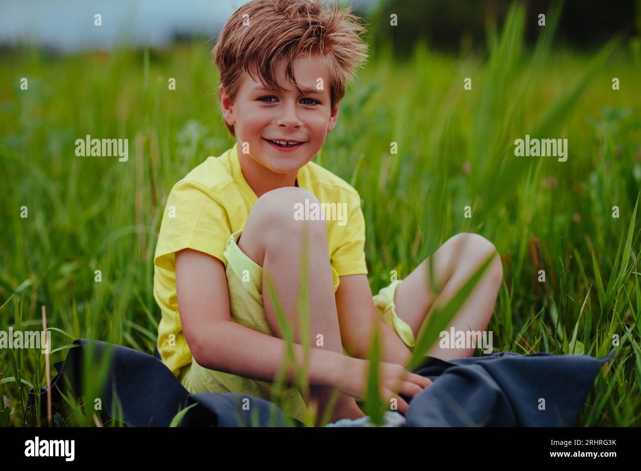 Glücklicher lächelnder Junge sitzt auf der grünen Wiese auf einem Handtuch Stockfoto