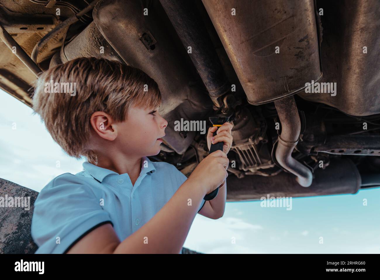 Junge Kfz-Mechaniker, der unter dem Boden des Fahrzeugs mit Schraubenschlüssel steht und das Fahrzeug repariert Stockfoto