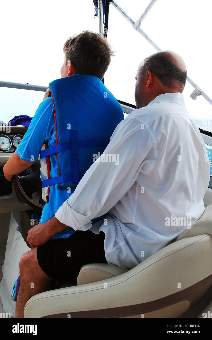 Ein Vater gibt seinem Sohn Bootsunterricht, während sie an einem Sommertag die Gewässer der Bucht vor der Küste von Long Island befahren Stockfoto