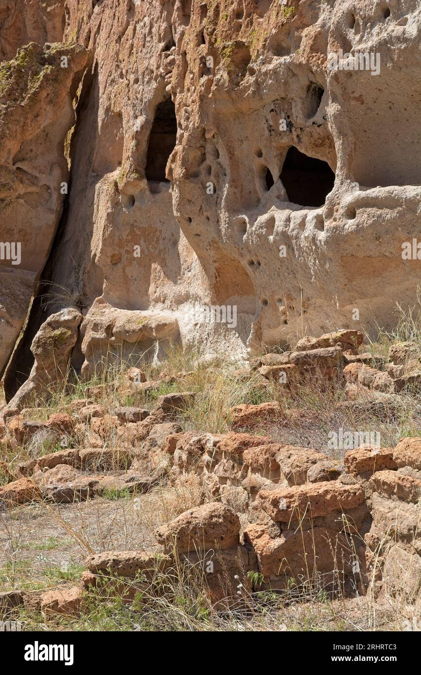 Ruinen aus Steinfundamenten vor Alkoven wie Höhlen, die von alten Bewohnern der Puebloan-Klippen in die vulkanischen Ascheebuff-beschichteten Canyon-Wände gehauen wurden Stockfoto