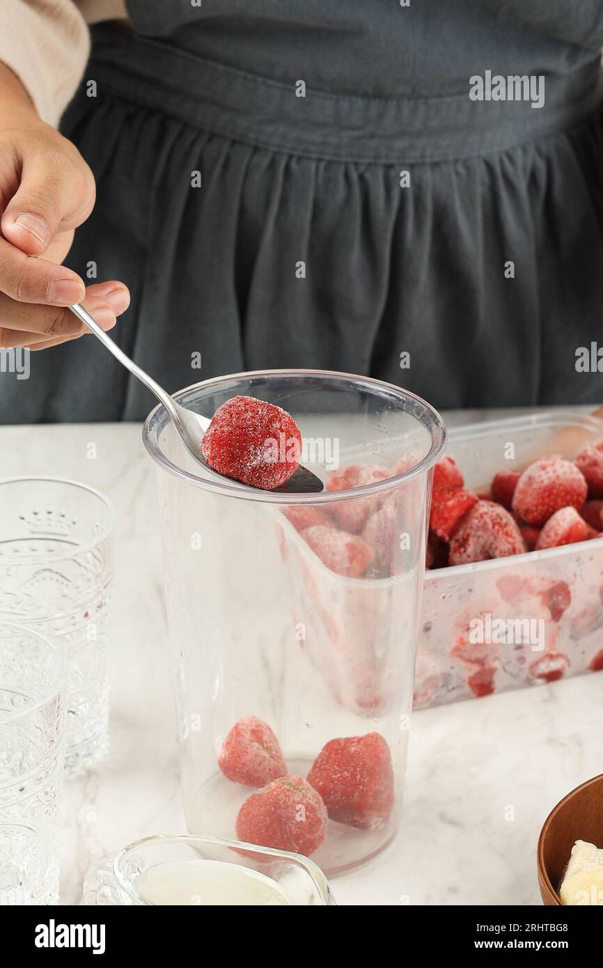Zubereitung Zubereitung von Erdbeersaft oder Slushy, weibliche Hand gefrorene Erdbeere in die Hand Entsafter Schüssel geben Stockfoto