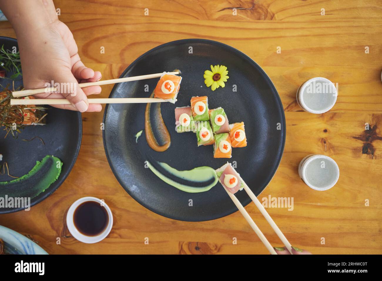 Essstäbchen, Hand und Essen Sushi und Essen in einem Restaurant für Ernährung am Tisch. Über hungrige Menschen mit Holzstöcken und Sojasauce zum Essen Stockfoto