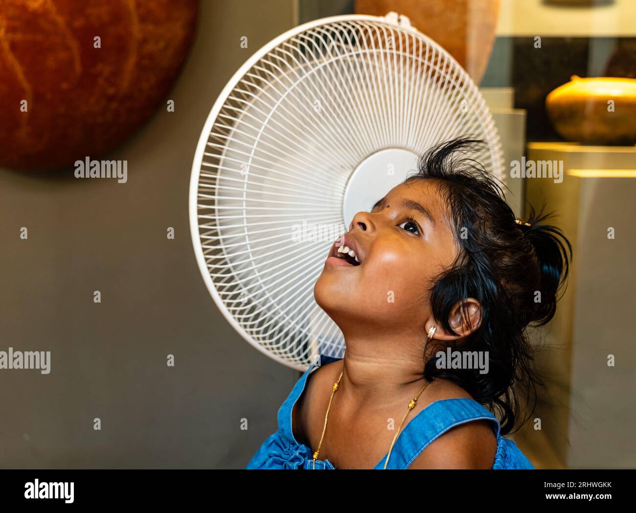 Ein junges Mädchen steht vor einem Tischventilator und genießt die kühle Luft Stockfoto