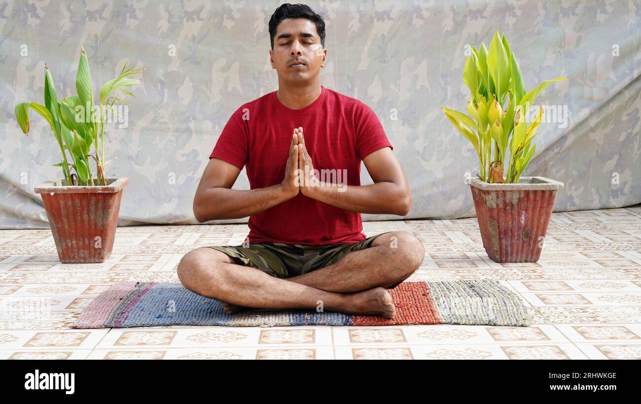 Junger Mann im sportlichen Outfit, der Yoga macht und auf einer Trainingsmatte vor Studiohintergrund meditiert Stockfoto
