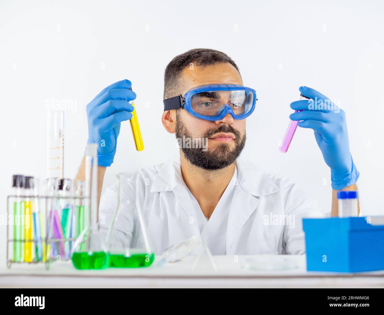 Ein männlicher Wissenschaftler, der eine Schutzbrille trägt, vergleicht zwei Flüssigkeitsproben in Reagenzgläsern Stockfoto