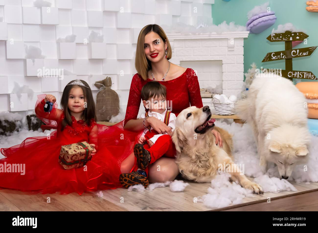 Familienfoto-Porträt. Mama und ihre zwei Kinder und zwei weiße Hunde in roten Kleidern feiern die Chistmas, Neujahr. Glückliche junge Mutter und ihre Tochter Stockfoto