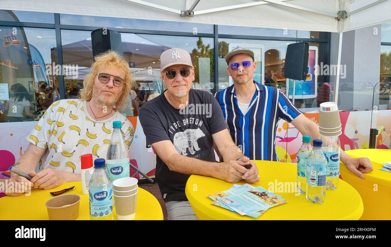 Hannover, Deutschland. August 2023. Christof Stein-Schneider (l-r), Gitarrist, Kai Wingenfelder, Sänger und Christian Decker, Bassist von der Band „Fury in the Smetzhouse“ signiert Autogramme vor dem Zweig einer Drogeriekette. Die sechs Mitglieder der Band "Fury im Schlachthof" sitzen für eine Stunde an der Kasse einer Drogerie für einen guten Zweck. Die Drogerie spendet den gesamten Erlös für die jährliche Weihnachtsfeier für Obdachlose und Bedürftige in Hannover. Quelle: Fernando Martinez/TNN/dpa/Alamy Live News Stockfoto