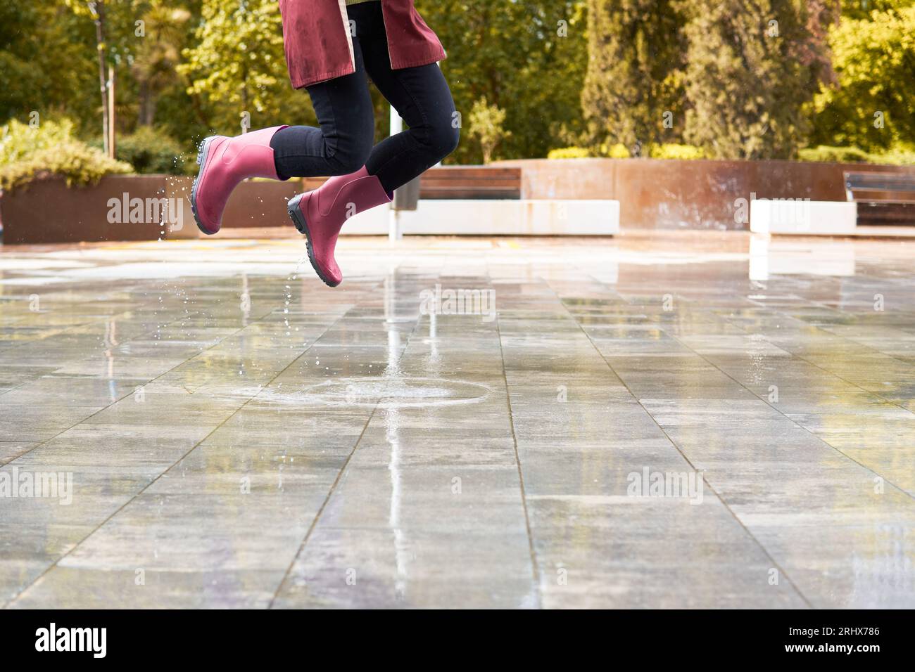 Glückliche Frau mit Stiefeln springt in einer Regenpfütze Stockfoto
