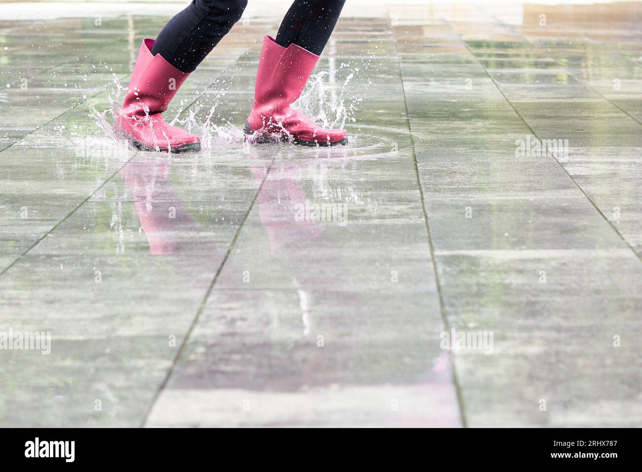 Glückliche Frau mit Stiefeln, die in einer Regenpfütze platschen Stockfoto