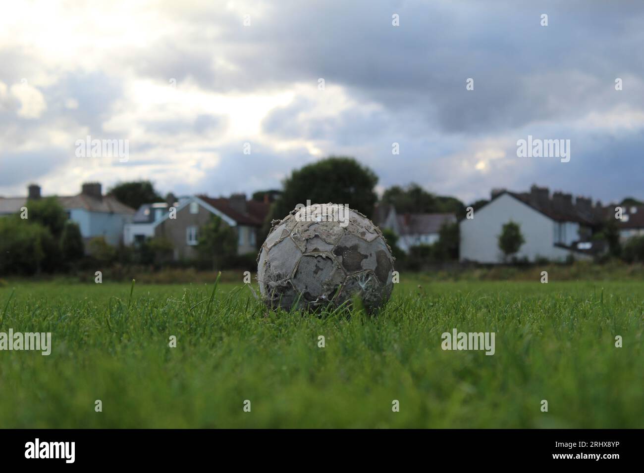 Ein Foto eines alten Fußballs auf einem grasbewachsenen Feld mit Häusern im Hintergrund. Stockfoto