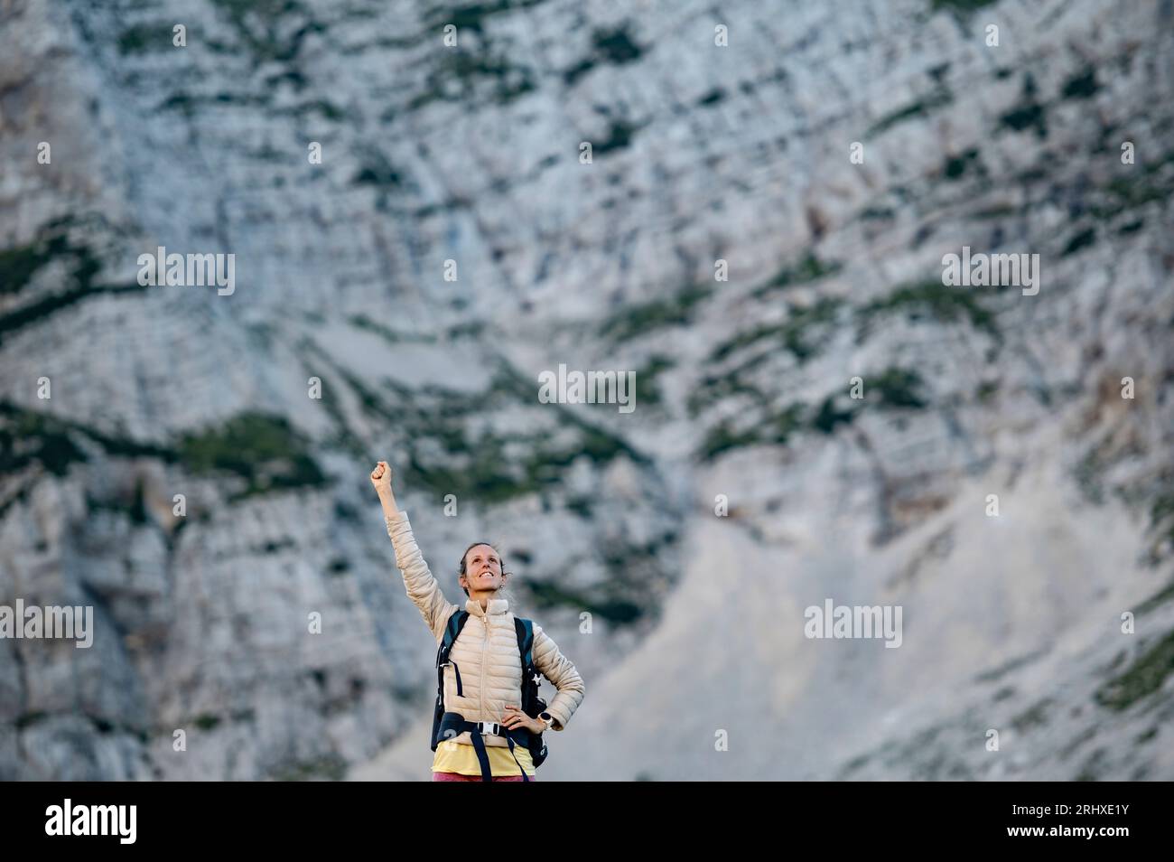 Glückliche junge Wanderin mit einem erhobenen Arm im Sieg. Mit hohen felsigen Bergen im Hintergrund. Stockfoto
