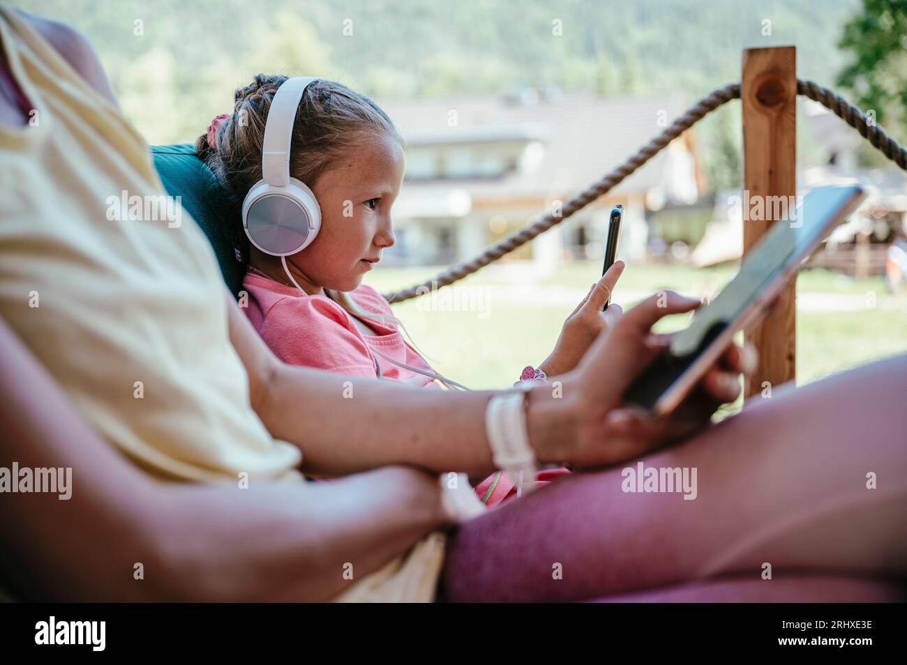 Probleme und Fallen moderner Technik und sucht - Profilansicht eines Kleinkinds mit Kopfhörern und ihrer Mutter, die in einem Café mit und sitzt Stockfoto