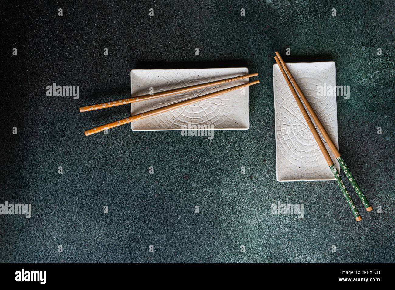 Von oben aus dem Set von weißen Keramikplatten auf schwarzem Betontisch mit Stäbchen im asiatischen Restaurant Stockfoto