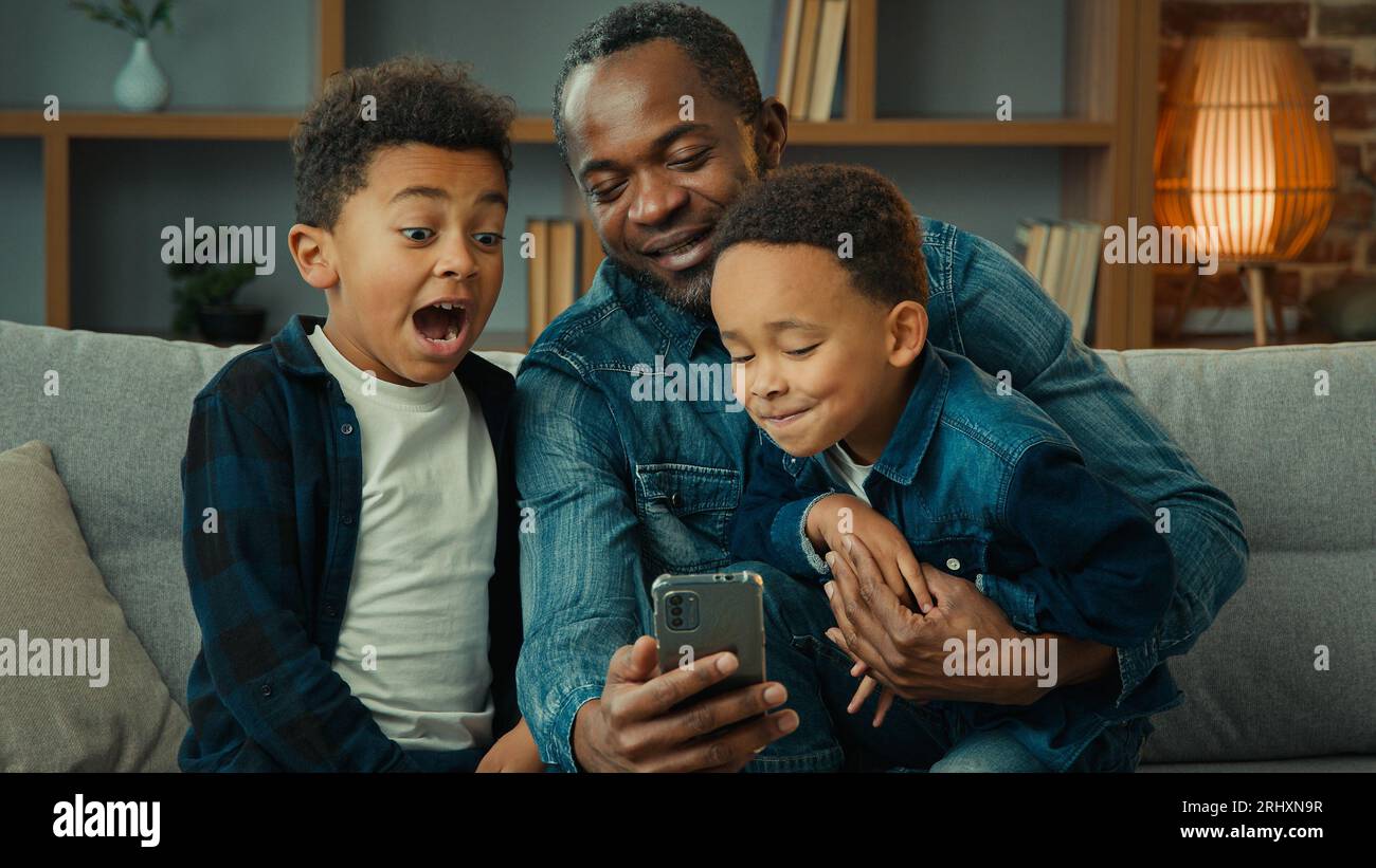 Afroamerikaner Vater Mann mit kleinen Jungen Kinder sitzen zusammen auf Sofa Sofa Sofa mit Smartphone Handy Video online sehen Vater mit Stockfoto