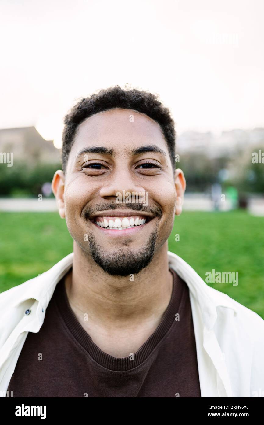 Vertikal lächelndes Porträt eines jungen Gen z-Mannes, der draußen auf die Kamera schaut. Stockfoto