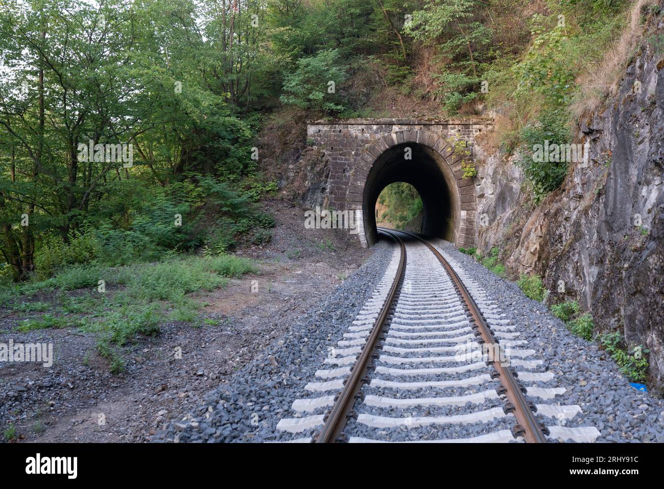 Ein kurzer Eisenbahntunnel unter einem grünen felsigen Hügel mit einer in Betrieb genommenen, renovierten Strecke. Linie 147 Beroun-Rakovník, in der Nähe der Stadt Roztoky u Křivoklátu. Stockfoto