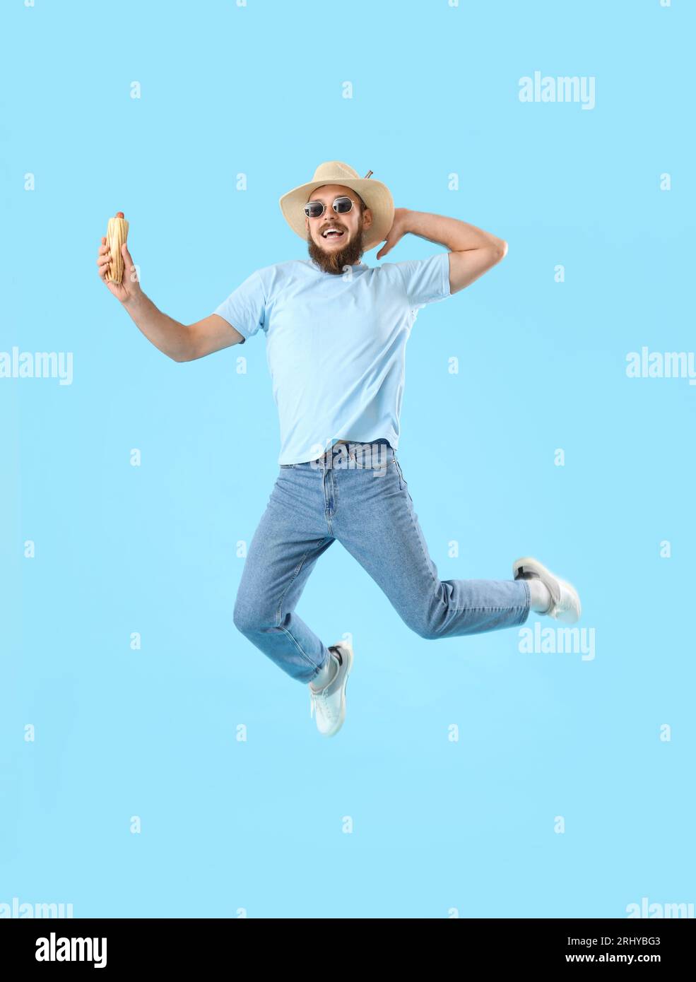 Schöner junger Mann, der mit leckerem Hot Dog auf blauem Hintergrund springt Stockfoto