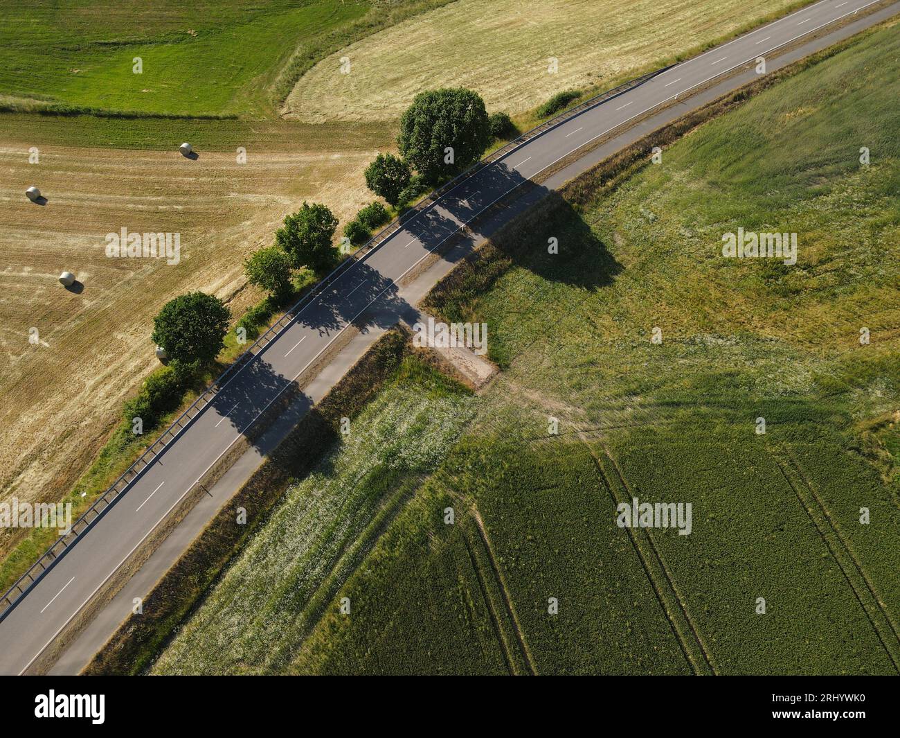 Drohnenansicht einer Straße in der Landschaft zwischen gemähten Grasfeldern und Bäumen Stockfoto