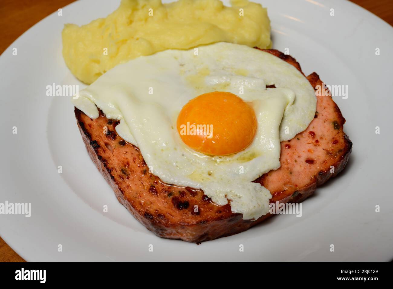 Gebratene, scharfe Leberkase mit gebratenem Ei, sonniger Seite nach oben und Kartoffelpüree auf einem weißen Teller Stockfoto
